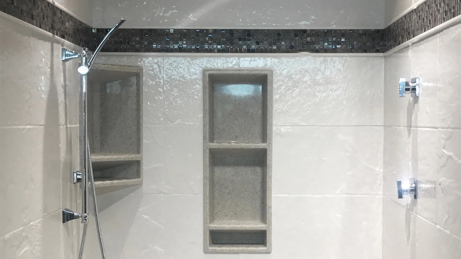 Modern Onyx shower with sleek wall-mounted faucets and integrated shelving against a tiled background with decorative mosaic accent.