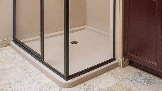 Light beige Onyx shower pan with a central drain, framed by a dark metal shower door frame. 
