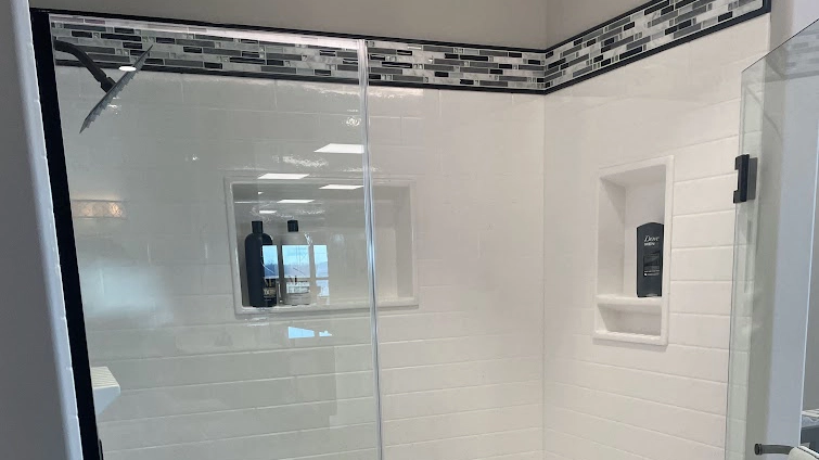 A sleek and modern corner shower with white subway tiles and an accent border of black and grey mosaic tiles at the top.