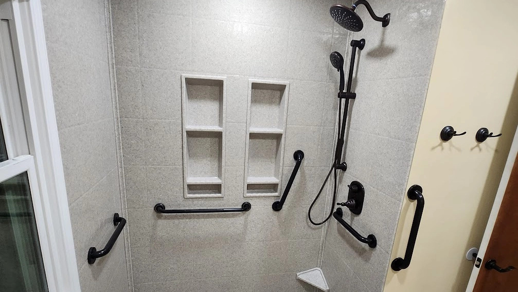 A functional and accessible bathroom shower area with light grey Onyx wall panels. The shower includes multiple black safety grab bars installed at various heights and positions for accessibility. 