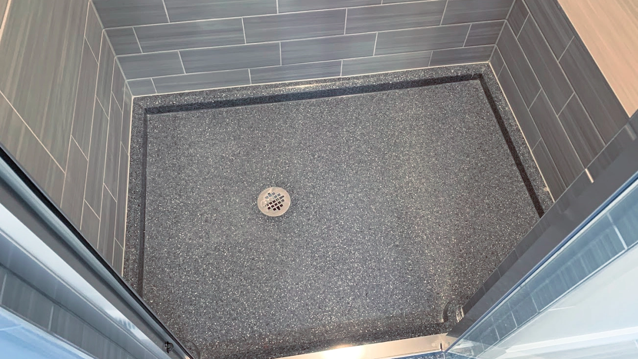 Modern Onyx shower pan, featuring a dark speckled surface with a central round drain. The pan is bordered by a low-profile curb that matches the wall tiles.